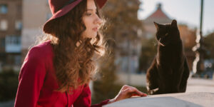 femme chic et élégante portant un chapeau et une veste rouge et discutant avec son chat noir