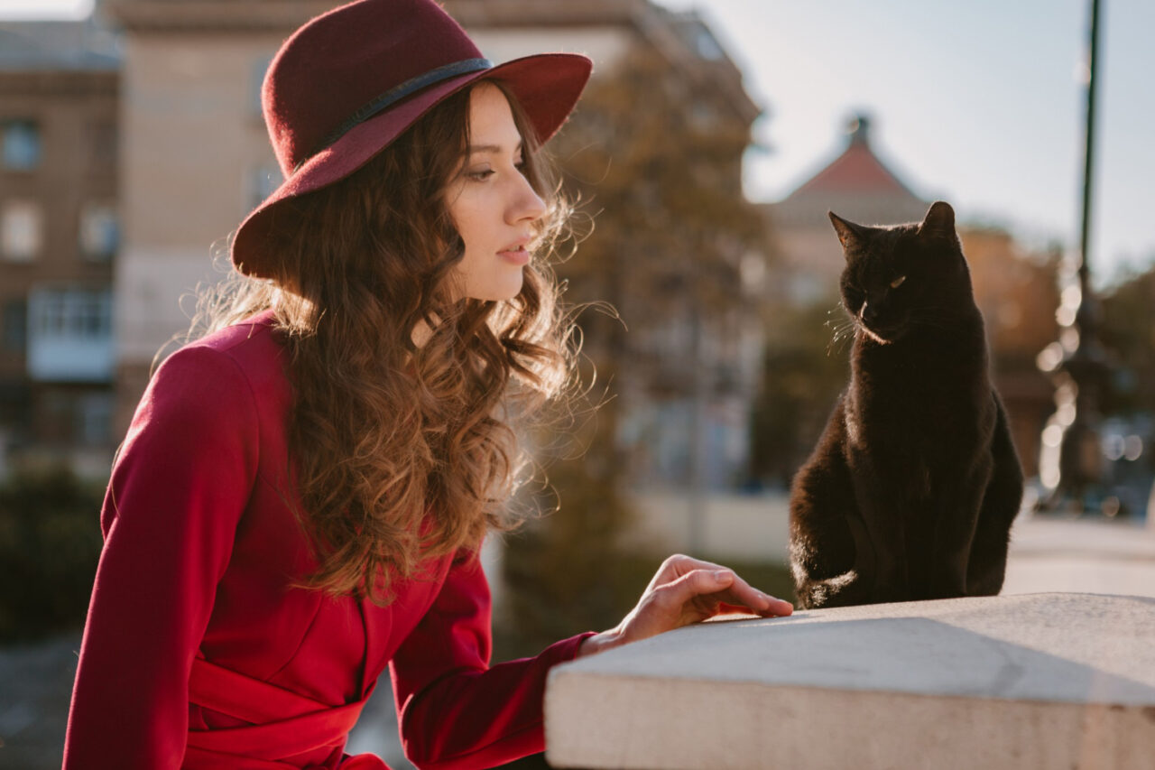 femme chic et élégante portant un chapeau et une veste rouge et discutant avec son chat noir